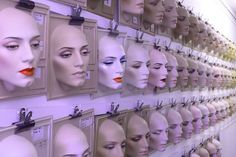 many mannequin heads are lined up on the wall