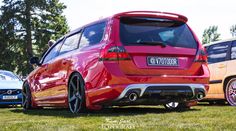 the rear end of a red car parked on top of a grass field next to other cars