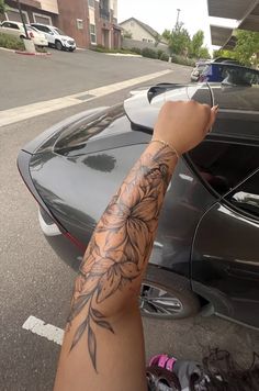 a person with a tattoo on their arm next to a parked car in a parking lot