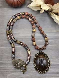 Hand-strung and hand-designed agate, jasper and wood beaded necklace with beautiful brown agate stone pendant and an antique bronze leaf toggle clasp. Handmade in Southwest Florida. Rustic Brown Pendant Jewelry, Bronze Jewelry With Wooden Beads For Gift, Vintage Brown Agate Necklace, Brown Vintage Agate Necklace, Rustic Brown Necklaces With Natural Stones, Rustic Bronze Beaded Jewelry, Nature-inspired Hand-strung Brown Jewelry, Rustic Brown Agate Jewelry, Nature-inspired Brown Hand-strung Jewelry