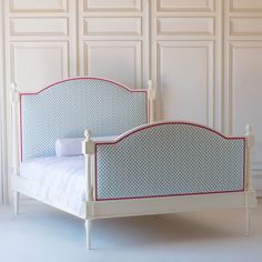 a white bed with blue and red trim on the headboard is against a wall