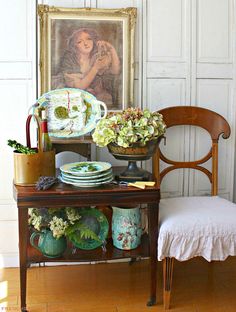 a table topped with plates and vases next to a painting