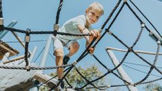 a young boy climbing up the side of a roped in play structure with ropes