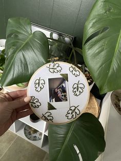 a person holding up a green leaf with a picture frame hanging from it's center