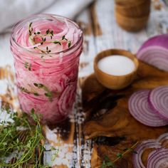 a jar filled with red onions next to sliced onion slices and herbs on a cutting board