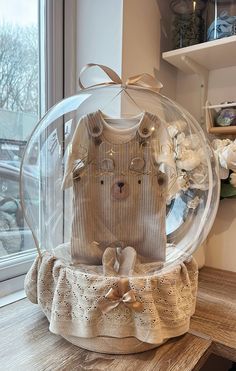 a teddy bear in a sweater under a clear glass ball on a wooden table next to a window