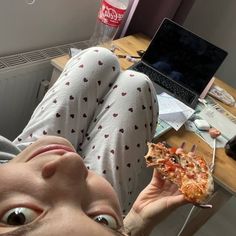 a woman is holding up a piece of pizza in front of her face and looking at the camera