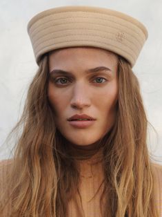 a woman with long blonde hair wearing a beige beret and looking at the camera