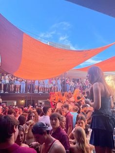 a woman standing in front of an audience at a music festival with orange tarps