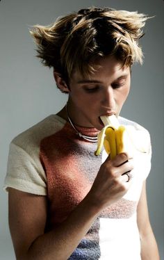 a young man eating a banana while wearing a necklace