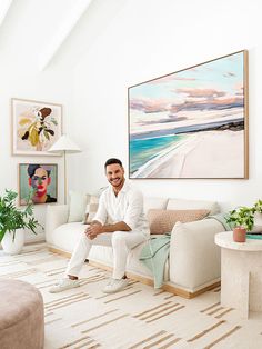 a man sitting on top of a couch in a living room next to a painting