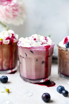 three desserts with blueberries and whipped cream in them are on a table next to flowers