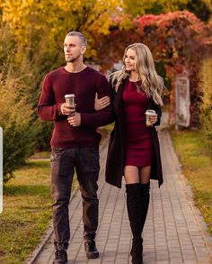 a man and woman walking down a sidewalk with coffee in their hands, both wearing boots