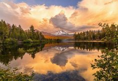 a lake surrounded by trees with a mountain in the background and clouds reflecting on it