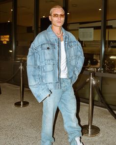 a man in blue jeans and white shirt standing next to an airport gate with his hands in his pockets