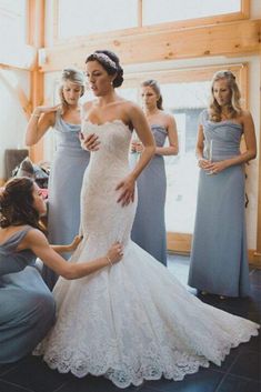 a woman in a wedding dress helping another woman put on her dress while others look on