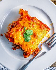 a piece of lasagna on a white plate with a fork and napkin next to it