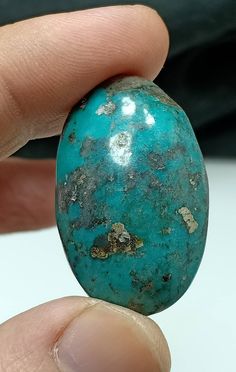 a person holding a turquoise colored stone in their left hand and the other hand is pointing at it