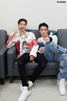 two young men sitting on a couch with their thumbs up