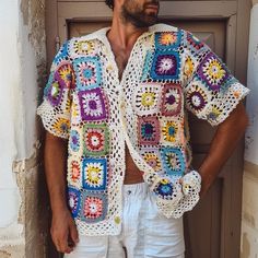 a man standing in front of a door wearing a crocheted shirt and white shorts