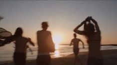 three people standing on the beach at sunset with their arms in the air and one person holding a frisbee