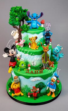 a three tiered cake with cartoon characters on it's sides and trees in the background