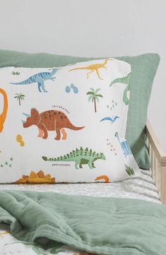 a bed topped with pillows covered in dinosaurs and dinos on it's sides