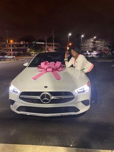 a woman standing next to a car with a pink bow on it