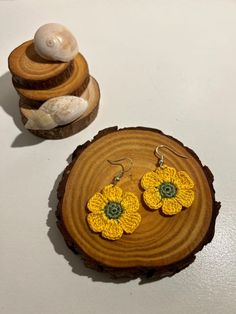 two yellow crocheted flower earrings sitting on top of a wooden slice next to a small container