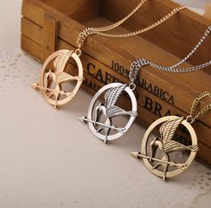 two necklaces that are sitting on top of a wooden box, one with an arrow and the other with a bird