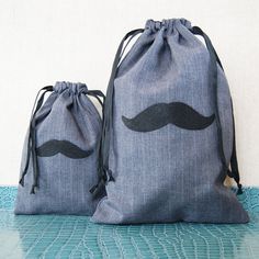 two drawstring bags with mustaches on them sitting on a blue tablecloth