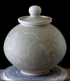 a large white vase sitting on top of a wooden table next to a black background