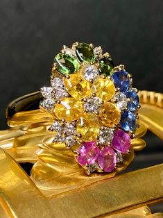 A dazzling and colorful cocktail ring done in 18K yellow gold set with buff-top natural blue, pink, green and yellow sapphires. Total approximate sapphire weight is 6.50cttw. Peppered throughout is another .70cttw in G-H color Vs2-Si1 clarity round diamonds. Dimensions/Weight: Ring measures .95" top to bottom and weighs 12.6g. Size 7 (sizable). Condition: All stones are secure and free of damage. Perfectly wearable condition. R-CNYE Luxury Multicolor Multi-stone Sapphire Ring, Multicolor Sapphire Ring In Fine Jewelry Style, Yellow Multi-stone Sapphire Ring, Multicolor Sapphire Multi-stone Ring, Multicolor Multi-stone Sapphire Ring, Multicolor Oval Sapphire Ring With Diamonds, Multicolor Sapphire Gemstone Ring, Multicolor Oval Sapphire Ring, Floral Cocktails