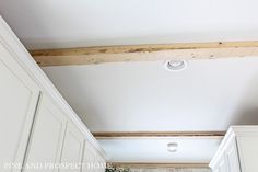 an empty kitchen with white cabinets and wood beams on the ceiling is seen in this image