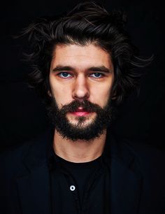 a man with long hair and a beard is looking at the camera while wearing a black shirt