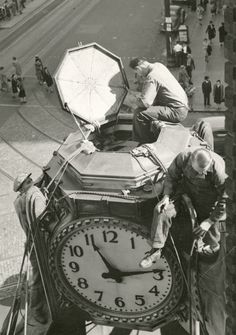 two men working on a large clock in the street