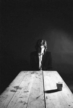 a man sitting at a wooden table with a cup in front of him and his shadow on the wall behind him