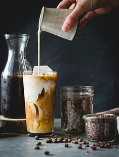 iced coffee being poured into a glass in front of two jars filled with beans and other ingredients