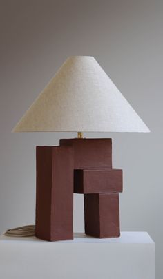 a lamp sitting on top of a table next to a brown block with a white shade