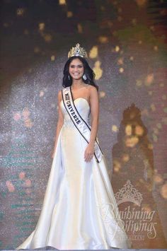 a beautiful woman in a white gown and tiara posing for a photo on the stage