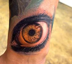 an eye tattoo on the leg of a person's arm, which is painted orange and black