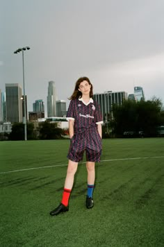 a woman standing on top of a lush green field next to a tall city skyline