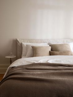 a bed with white sheets and pillows in a bedroom next to a lamp on a table