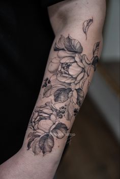 a woman's arm with flowers and leaves tattooed on the left side of her arm