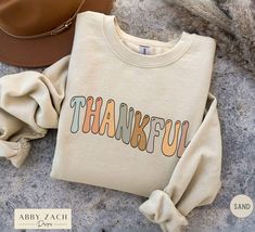 Celebrate all that you are thankful for with this playful and festive Thanksgiving Sweatshirt. We print on Gildan brand sweatshirts which are both soft and cozy. Also available as a t-shirt or hoodie option. To view all our Thanksgiving designs please visit our shop's homepage. https://www.etsy.com/shop/AbbyZachDesigns ----HOW OUR SHIRTS ARE MADE ----  * We use the process of DTG, which stands for direct to garment printing. We partner with a professional printer who applies ink directly into the shirt. (We do not use vinyl.) This gives you better quality and will not peel. ----PRODUCT INFORMATION ---- * Our sweatshirts and hoodies are printed on the Gildan 18000 and 18500 respectively. The fabric is medium heavy fabric that is both soft and plush. * Fabric content is 50% cotton and 50% po Comfortable Fit Text Print Sweatshirt For Fall, Trendy Pre-shrunk Fall Sweatshirt, Cute Thanksgiving Shirts Friends, Fall Sweatshirt With Text Print And Comfortable Fit, Thanksgiving Friends Shirt, Familt Thanksgiving Shirts, Thanksgiving Designs, Thankful Sweatshirt, Brand Sweatshirts