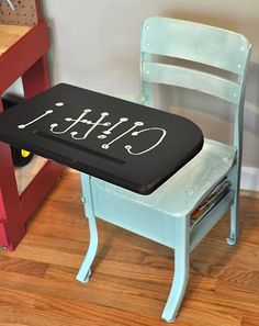 a small blue chair sitting next to a wooden table with writing on the back of it