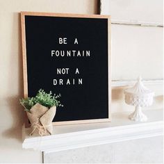 a black sign that says be a fountain not a drain with a plant next to it