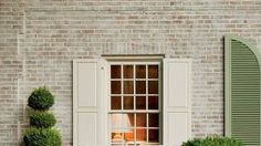 an open window with shutters and potted plants in front of it on the side of a brick building