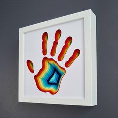 a colorful handprint on a white frame hangs on the wall next to a gray wall