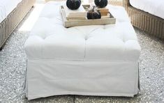 a white ottoman sitting on top of a stone floor next to two black vases